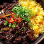 Crispy Chilli Beef Recipe bowl served with fluffy yellow rice, topped with sliced red chili, green onions, and sesame seeds in a sticky sweet-spicy sauce.