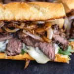Steak Sandwich Recipe with sliced steak, caramelized onions, and melted Havarti on a toasted baguette.