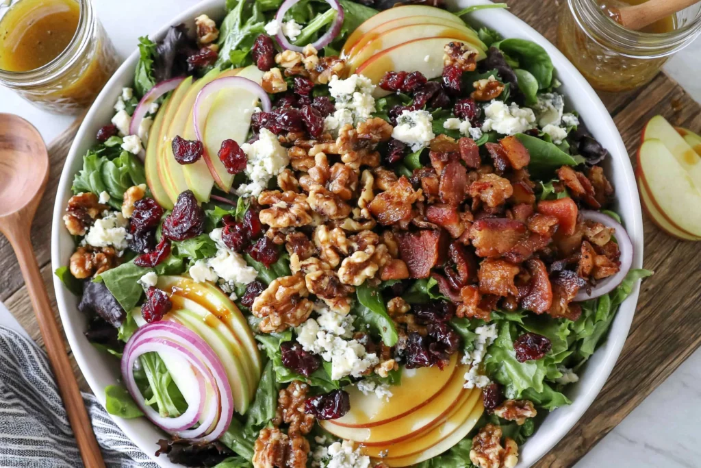 Blue Cheese Apple Walnut Salad topped with crispy bacon, candied walnuts, blue cheese crumbles, sliced apples, dried cranberries, red onion, and maple vinaigrette over fresh mixed greens.