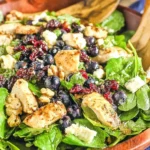 Chicken Blueberry Feta Salad in a wooden bowl with spinach, grilled chicken, blueberries, dried cranberries, walnuts, and feta with balsamic vinaigrette.