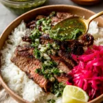 Skirt Steak Rice Bowls with Chimichurri Sauce with seared skirt steak over white rice, spooned cilantro chimichurri, pickled red onions, and a lime wedge.