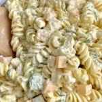 Dill Pickle Pasta Salad in a glass bowl with creamy dill dressing, rotini pasta, chopped dill pickles, fresh dill, and cheese cubes.
