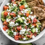 Avocado Feta Dip topped with crumbled feta, diced tomatoes, fresh parsley, and creamy avocado, served with crispy crackers.