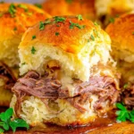 Close-up of French Dip Sliders on buttery Hawaiian rolls with tender roast beef, melted provolone, herbs, and au jus for dipping.