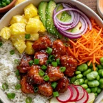Hawaiian Chicken Poke Bowl with sticky chicken, rice, pineapple, avocado, carrots, edamame, red onion, radishes, and spicy mayo.