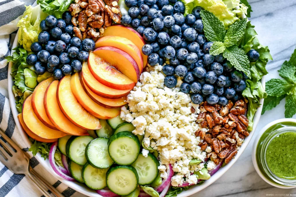 Peach Berry Summer Salad with fresh blueberries, sliced peaches, cucumber, feta cheese, pecans, and crisp lettuce served with homemade lemon basil dressing.