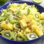 Pineapple Kiwi Salad in a blue bowl with fresh pineapple chunks, sliced kiwi, mint, lime, and toasted coconut.