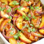 Roasted Peach BBQ Chicken Bake in a white baking dish with BBQ-glazed chicken, roasted peach slices, red onion, and fresh cilantro.