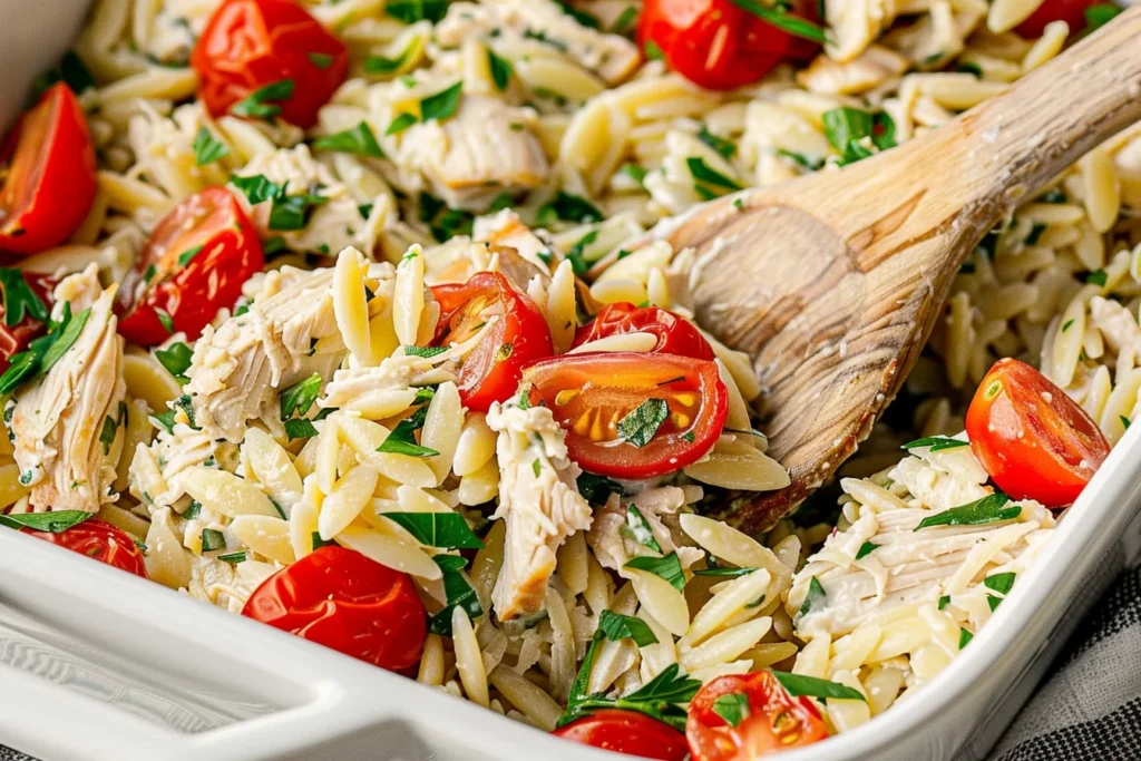 Close-up of Dump and Bake Chicken Orzo Bake with tender shredded chicken, orzo pasta, cherry tomatoes, and fresh parsley in a creamy casserole.