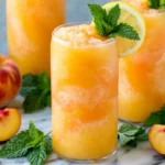 Peach Lemonade in a frosty glass garnished with fresh lemon slices, mint leaves, and ripe peaches for a refreshing summer drink.