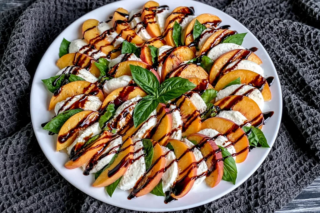 Peach Caprese Salad arranged with fresh peach slices, creamy mozzarella, basil leaves, and balsamic glaze on a white serving platter.