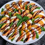 Peach Caprese Salad arranged with fresh peach slices, creamy mozzarella, basil leaves, and balsamic glaze on a white serving platter.