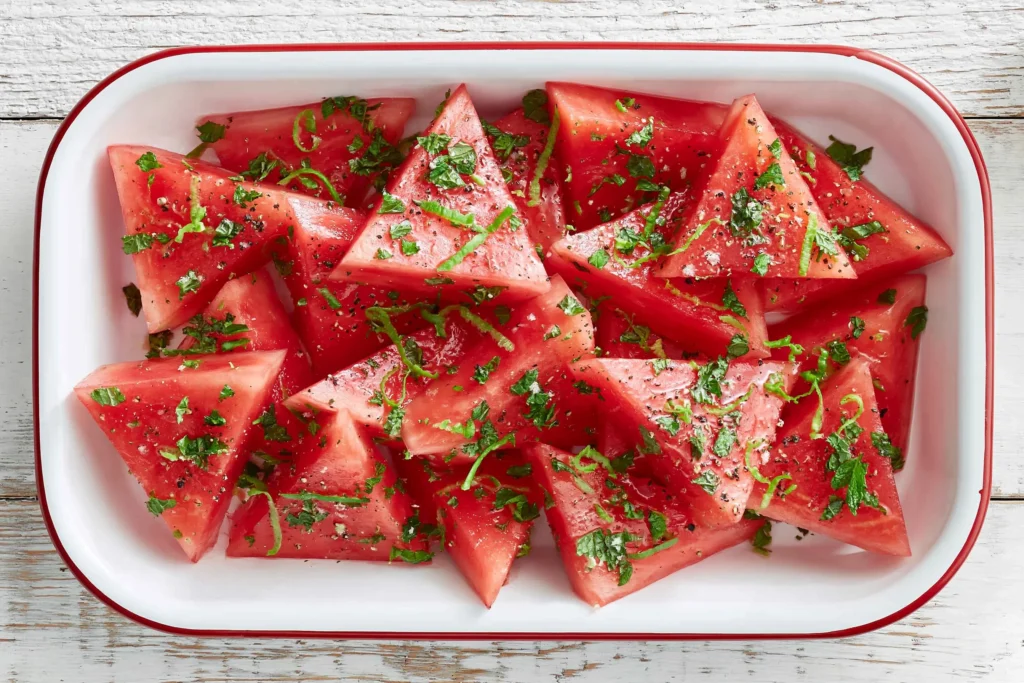 Mojito Watermelon topped with fresh mint, lime zest, and cracked black pepper, served chilled in a white baking dish.