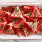 Mojito Watermelon topped with fresh mint, lime zest, and cracked black pepper, served chilled in a white baking dish.