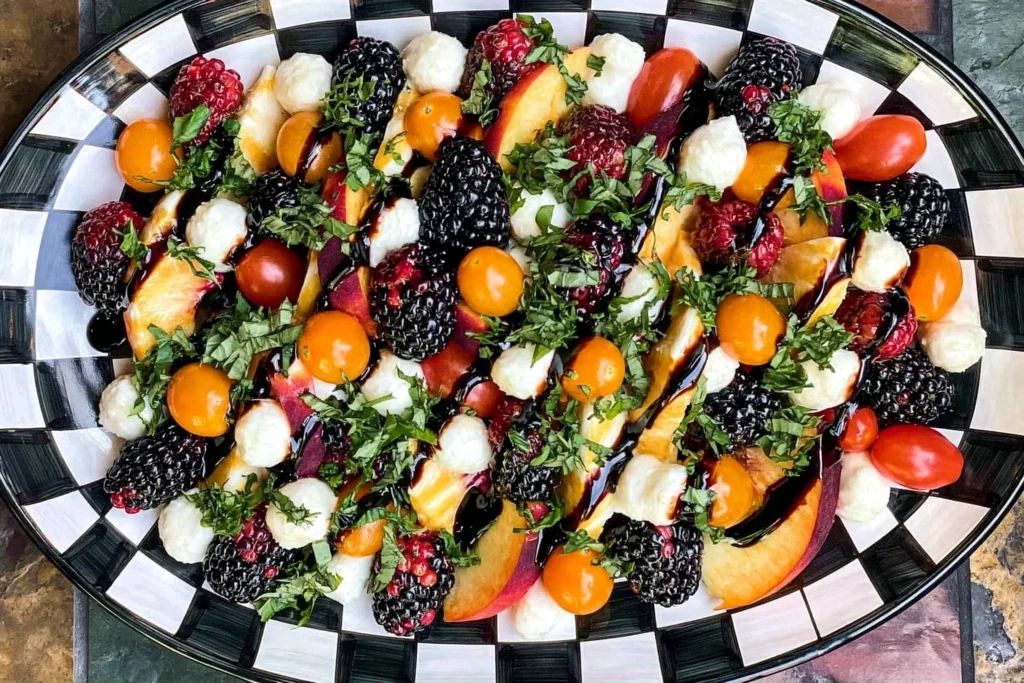 Summer Fruit Caprese Salad made with fresh peaches, cherry tomatoes, mozzarella pearls, blackberries, raspberries, basil, and balsamic glaze on a serving platter.