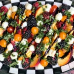 Summer Fruit Caprese Salad made with fresh peaches, cherry tomatoes, mozzarella pearls, blackberries, raspberries, basil, and balsamic glaze on a serving platter.