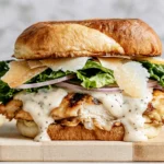Grilled Chicken Caesar Burger with grilled chicken, creamy Caesar dressing, shaved Parmesan, crisp romaine lettuce, red onion, and a toasted brioche bun.