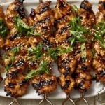 Honey Garlic Asian Chicken Kabobs with caramelized grill marks, sesame seeds, and sliced green onions on a white platter